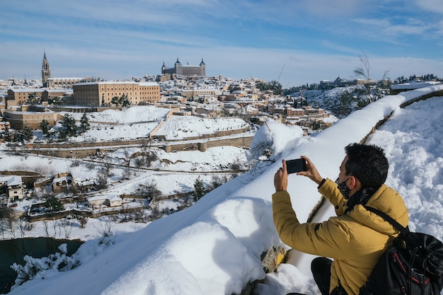 Persoon met gele jas die een foto maakt met de mobiel van Toledo Spanje besneeuwd