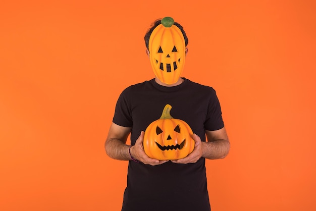 Persoon met pompoenmasker die Halloween viert met een pompoen op een oranje achtergrond Concept van viering Allerzielen en Allerheiligen
