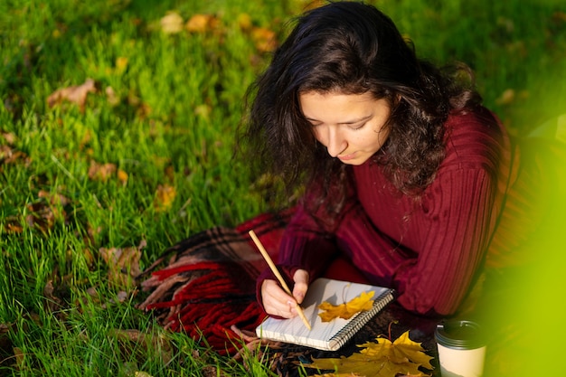 Persoon schrijft notities liggend op het gazon in het herfstpark. Eenzaamheid met jezelf.