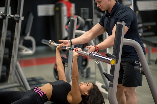 Persoonlijke trainer die de pers van de vrouwenbank in gymnastiek helpen