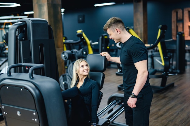 Persoonlijke trainer die een jonge vrouw helpt met het gebruik van de oefenmachine in de sportschool