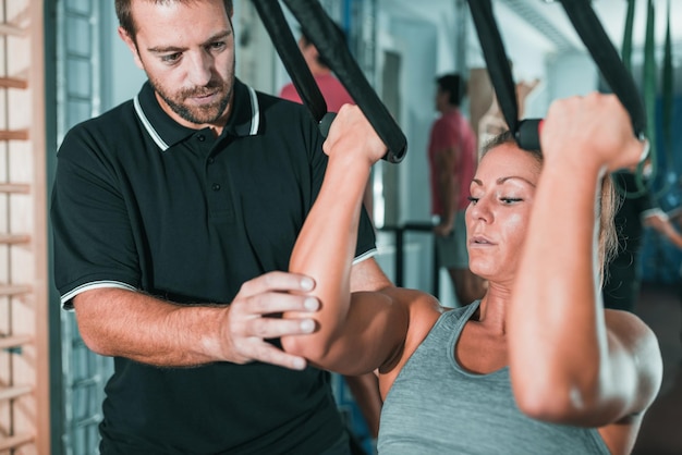 Persoonlijke trainer oefent op TRX met een vrouw in de sportschool
