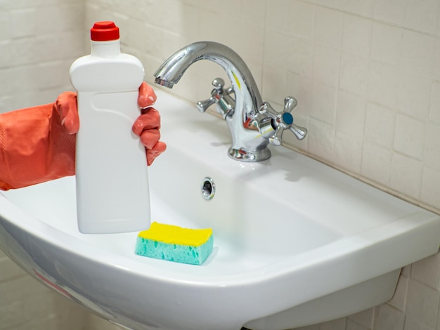 Persoonshand die een wasmiddel in witte fles houdt voor het schoonmaken van badkamersgootsteen