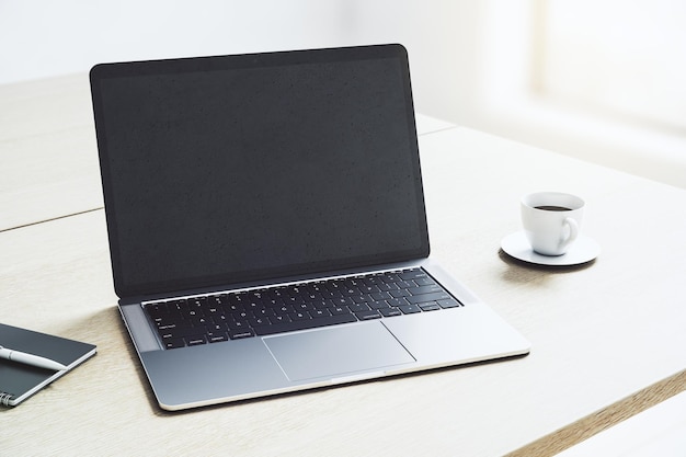 사진 밝은 사무실 공간 3d 렌더링 모형에 커피 머그가 있는 밝은 나무 테이블에 로고 또는 텍스트를 위한 카피스페이스가 있는 빈 어두운 현대 노트북 화면의 원근 보기