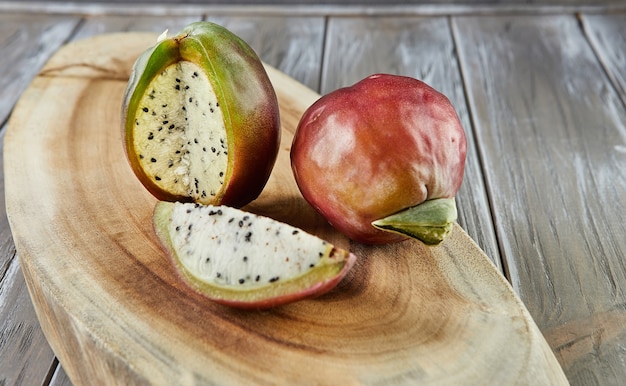 Peruvian apple cactus fruits whole and cut on wooden stand on gray board. Scientific name Cereus repandus