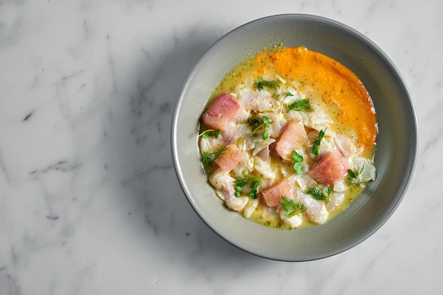 Photo peruvian cuisine dish. seabass ceviche with grapefruit and yellow sauce, served in a grey plate on marble