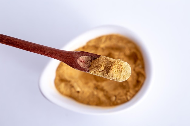 Peruvian maca powder with rustic wooden spoon on a white background selective focus