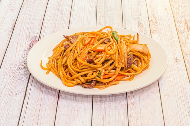 Peruvian recipe of sauteed noodles with beef tenderloin onion and red and green peppers some carrot and soy sauce on a white tray