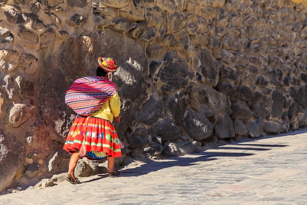 사진 페루 여자 cholita는 자루를 들고 돌담으로 된 거리를 걸어가는 전통적인 화려한 천을 입은 inkan sacred valley ollantaytambo peru