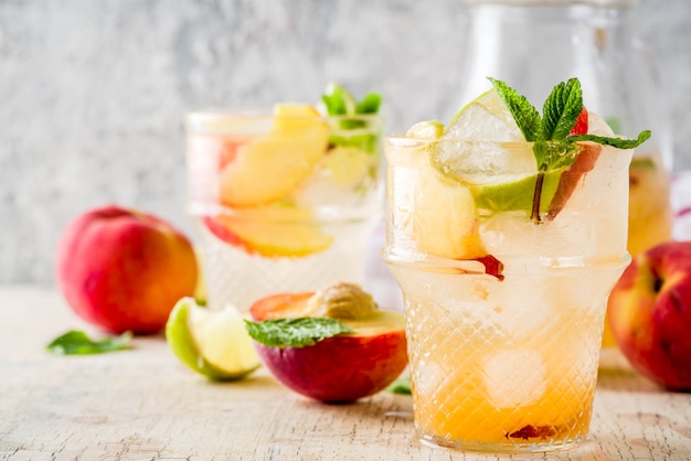 Perzik en limoen limonade, mojito cocktail met vers fruit garnituur, om lichte betonnen tafel