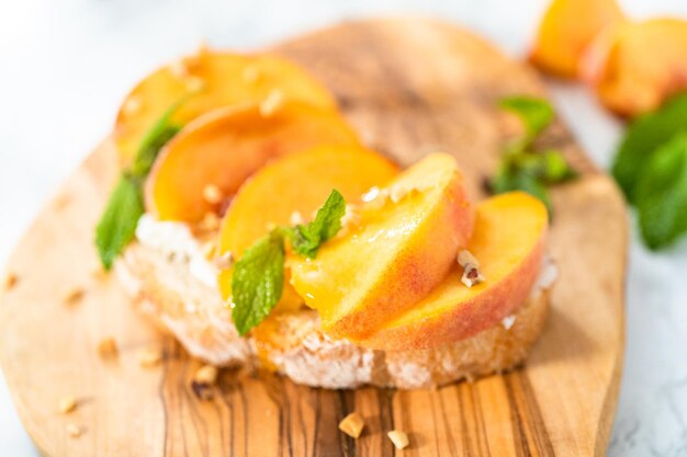 Perzik ricotta toast gegarneerd met walnoten en verse munt op een houten snijplank.