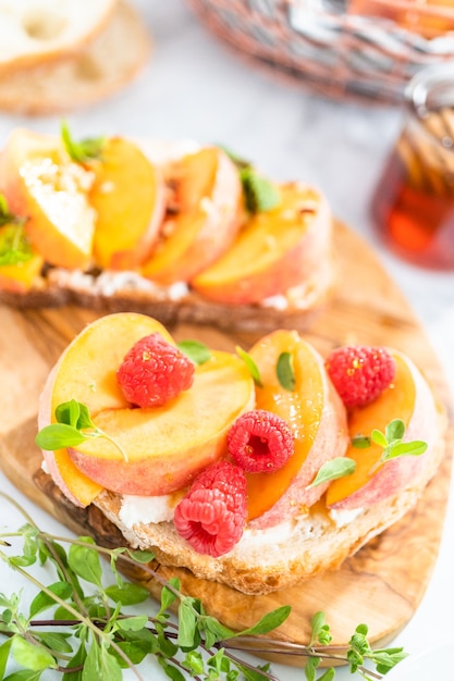 Perzik ricotta toast gegarneerd met walnoten, verse munt en frambozen op een houten snijplank.