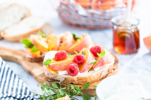 Perzik ricotta toast gegarneerd met walnoten, verse munt en frambozen op een houten snijplank.