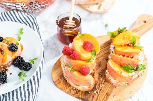 Perzik ricotta toast gegarneerd met walnoten, verse munt en frambozen op een houten snijplank.