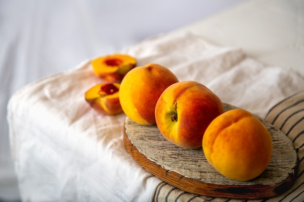 Perziken op tafel in de keuken bij het raam. Rustiek minimalisme eten perzik fruit met bladeren op een houten bord op tafelkleed. Oogst van rijpe sappige perziken. Lange webbanner.