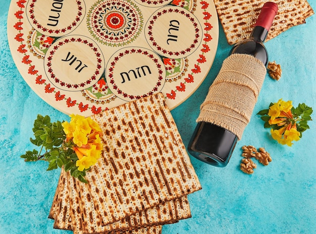 Фото Концепция празднования песаха еврейский праздник песах фон с желтыми цветами с бокалом винной мацы и тарелкой седера на синем фоне традиционные надписи на иврите на тарелке