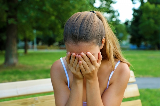 Pesten, discriminatie of stressconcept. trieste tiener die alleen in het park huilt. boos jonge vrouwelijke student met angst.