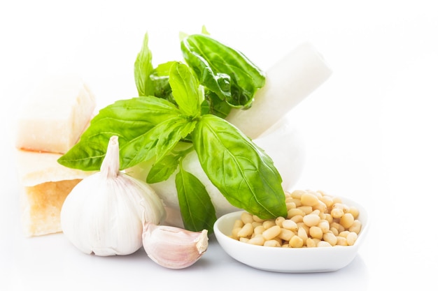 Ингредиенты для соуса песто, свежий зеленый базилик, пармезан, кедровые орехи и чеснок. На белом