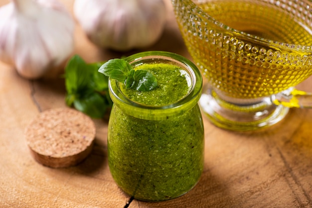 Pesto sauce. In a transparent glass with the ingredients in the background. Olive oil, garlic and basil.