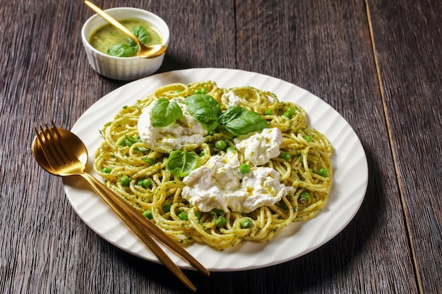 녹색 완두콩을 얹은 페스토 스파게티, 찢어진 모짜렐라 볼을 얹은 신선한 바질 잎을 접시에 담은 이탈리아 요리