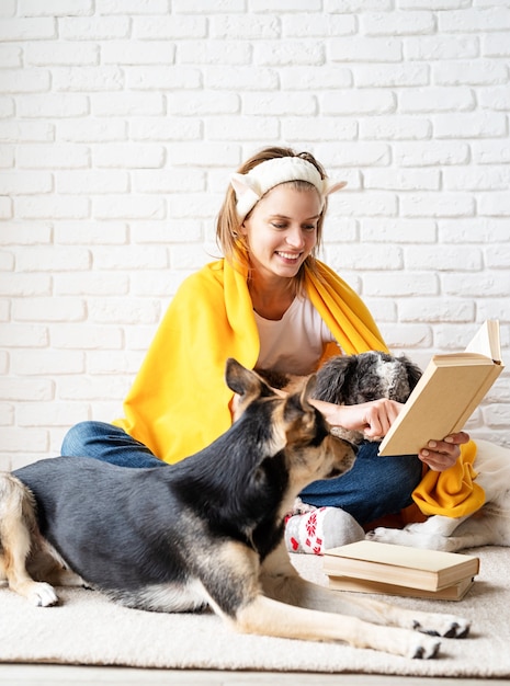 Cura degli animali. giovane donna sorridente divertente in plaid giallo che si siede con i suoi cani che leggono un libro