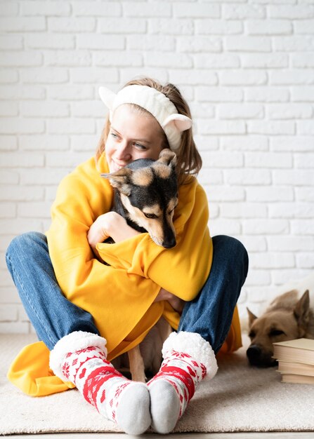 Уход за животными. Смешная молодая женщина в желтом пледе сидит на полу, обнимая свою собаку