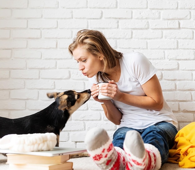 Photo pet care funny young woman in yellow plaid sitting on the floor with her dogs drinking coffee