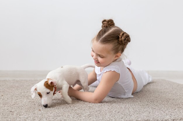 ペット、子供時代、動物のコンセプト-子犬ジャックラッセルテリアと床で遊んでいる小さな子供の女の子