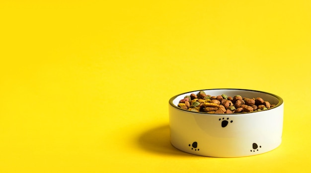 Pet food bowl with dry granulated food on a yellow background