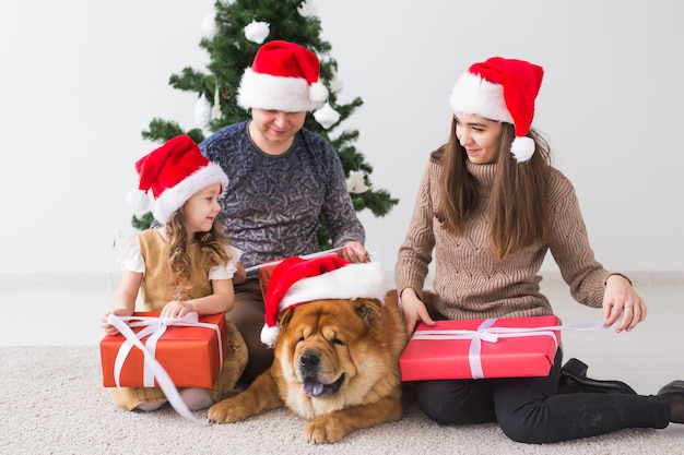 ペット、休日、お祭りのコンセプト-犬と一緒に家族がクリスマスツリーの近くの床に座っています。