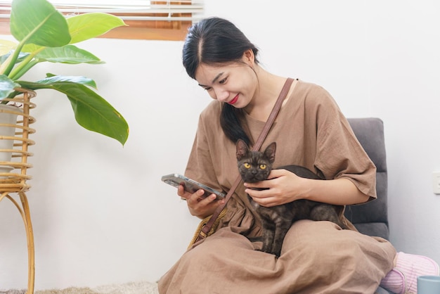 Pet lover concept Jonge Aziatische vrouw die smartphone gebruikt en met kat speelt terwijl ze thuis ontspant