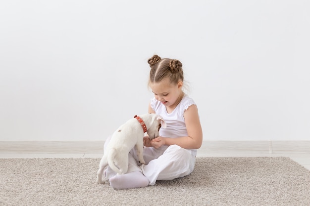 ペットの飼い主、子供と犬のコンセプト-かわいいジャックラッセルテリアの子犬と一緒に床に座って遊んでいる小さな女の子
