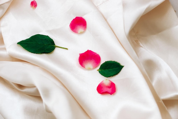 Petals of pink roses on a white silk background with space for text