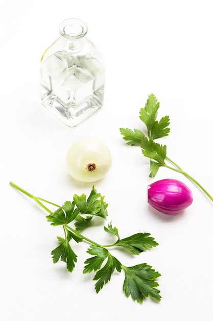 Peterselieblaadjes, twee koppen witte en blauwe uien. Glazen fles met water. Witte achtergrond.