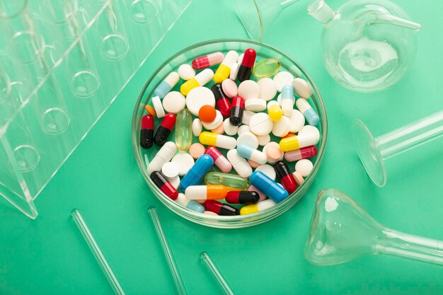 Petri dish with a bunch of pills and tweezers along with a syringe on a blue background