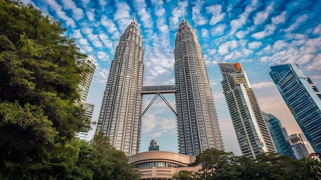 Photo petronas twin towers near skyscrapers and trees under a blue sky in kuala lumpur malaysia