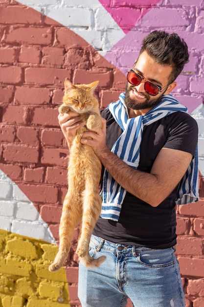 Pets and animals concept - Handsome young man with cute red cat outdoors