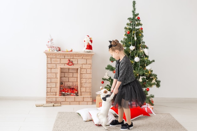 Animali domestici, vacanze e concetto di natale - bambina che gioca con il cucciolo jack russell terrier vicino all'albero di natale.