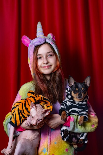 애완 동물과 소유자. 소녀, 고양이 및 빨간색 배경에 그녀의 개. 고양이와 강아지를 품에 안고 있는 소녀.