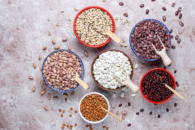 Peulvruchten en bonen assortiment in verschillende kommen op lichte stenen achtergrond. bovenaanzicht gezond veganistisch eiwitvoer.