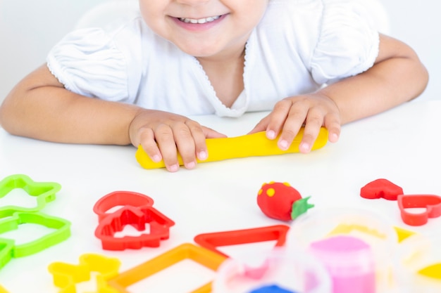 Peuter beeldhouwt van gekleurde plasticine op een witte tafel