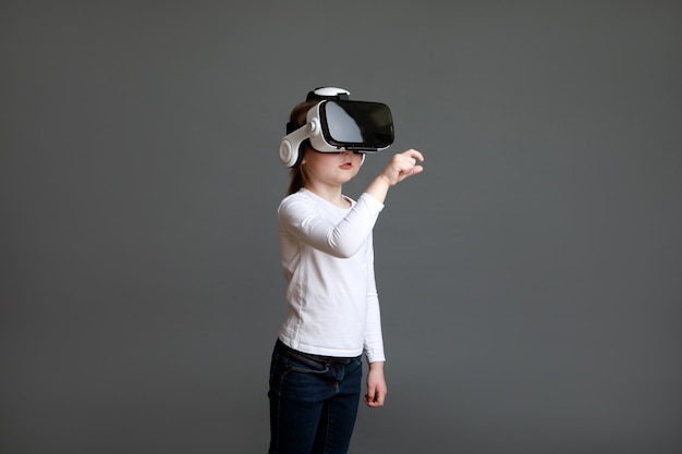 Peuter meisje ervaart virtual reality lenzenvloeistof in wit shirt met lange mouwen over grijs oppervlak.