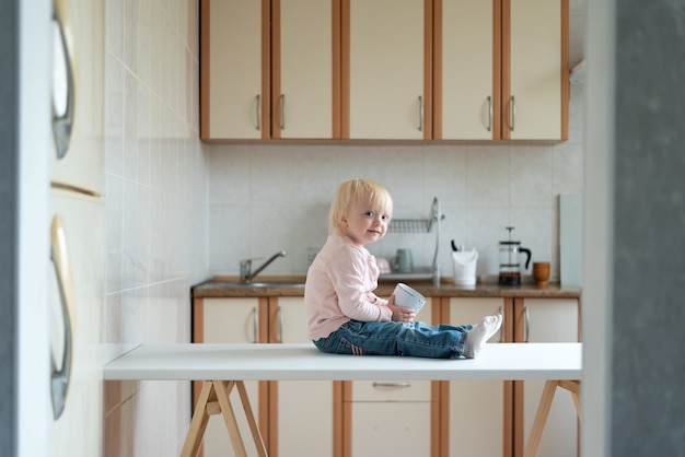 Peuter zit op de keukentafel en wacht op moeder. Thuis ontbijt.