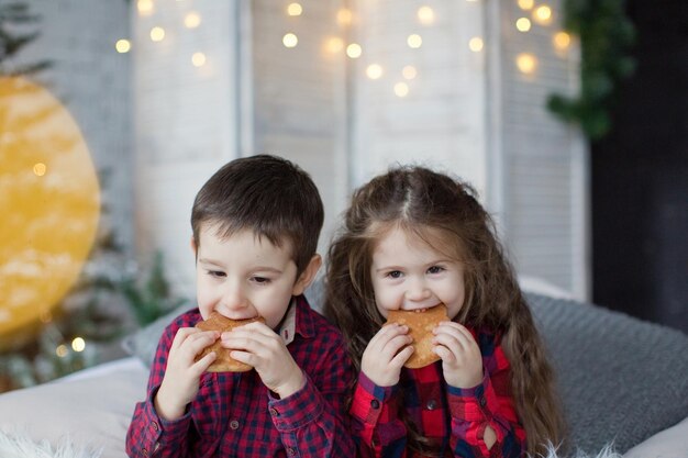 Peuterjongen en -meisje in rode shirts eten koekjes bij de kerstboom Leuke kerstkinderen