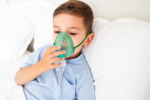 Foto peuterjongen ligt ziek in bed met een masker voor inademing