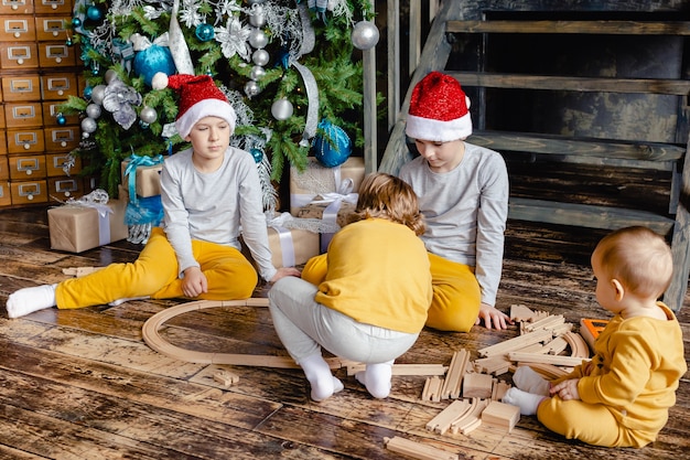 Peuterjongens met kerstmuts bouwen spoorweg en spelen met speelgoedtrein onder de kerstboom. Kinderen met kerstcadeaus. Kersttijd.