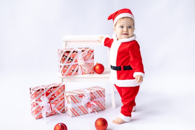 Peuterkind in een kerstmankostuum staat met geschenken op een witte achtergrond nieuwjaarskerstmis