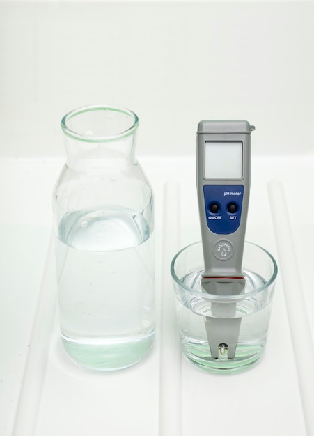 pH-meter in een glas water en fles op een witte en witte achtergrond