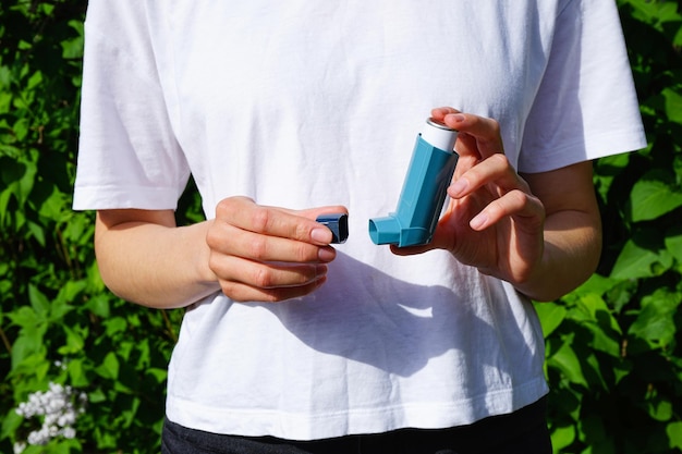 Pharmaceutical drug for the relief of an asthma attack Hands of a young woman holding a blue asthma inhaler outdoors Health and medical concept