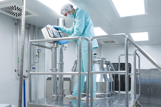 Pharmaceutical factory man worker in protective clothing operate production line in sterile working conditions